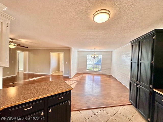 kitchen with crown molding, a textured ceiling, wooden walls, light tile patterned floors, and ceiling fan with notable chandelier