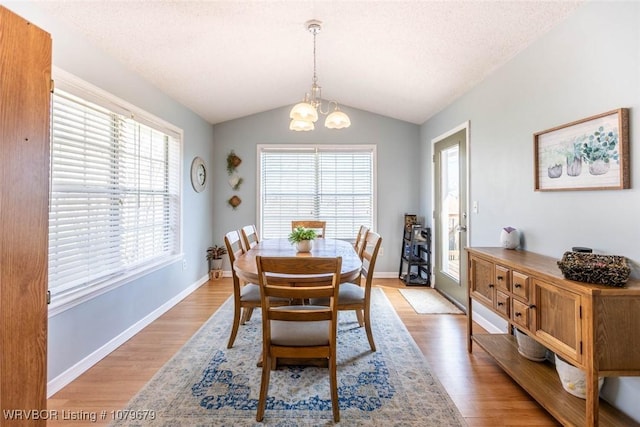 dining area with a notable chandelier, light wood-style flooring, a textured ceiling, and vaulted ceiling