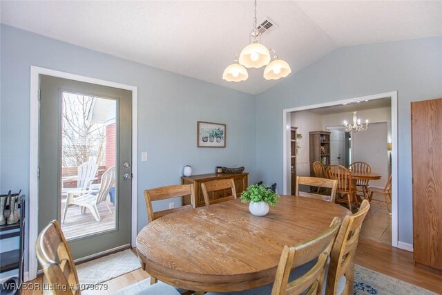 dining area with visible vents, light wood-style floors, an inviting chandelier, baseboards, and vaulted ceiling
