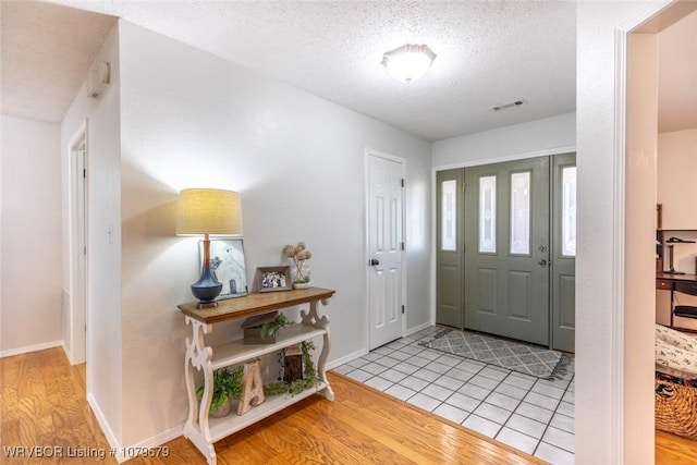 entrance foyer with baseboards, visible vents, light wood finished floors, and a textured ceiling
