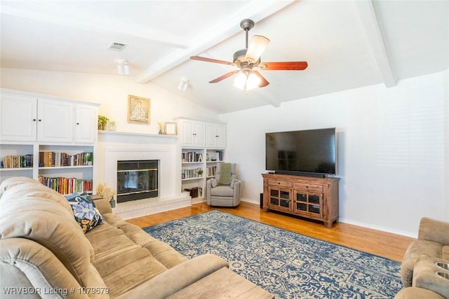 living area with a glass covered fireplace, ceiling fan, lofted ceiling with beams, and light wood-style floors