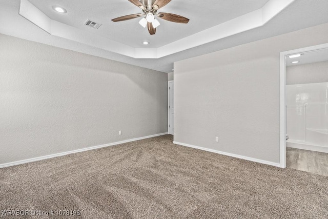 carpeted empty room with ceiling fan and a tray ceiling