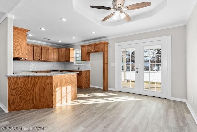 kitchen with a raised ceiling, kitchen peninsula, decorative backsplash, a wealth of natural light, and french doors