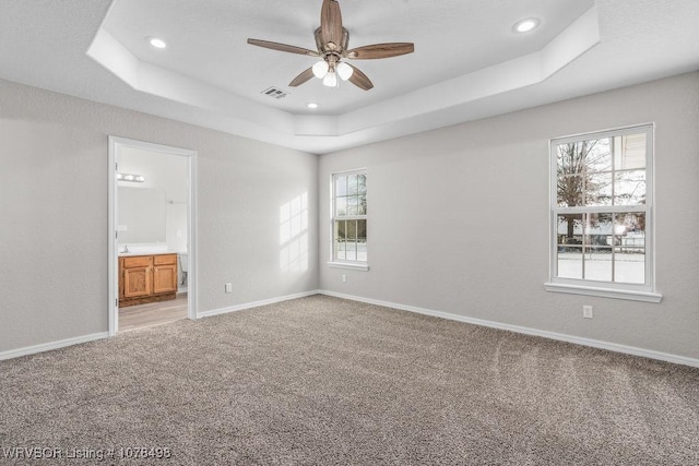 empty room with plenty of natural light, a tray ceiling, and light carpet