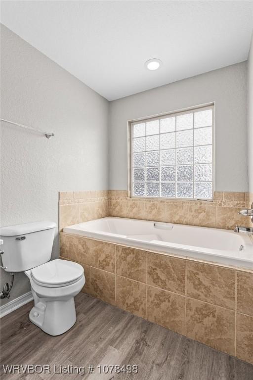 bathroom with toilet, tiled bath, and hardwood / wood-style flooring