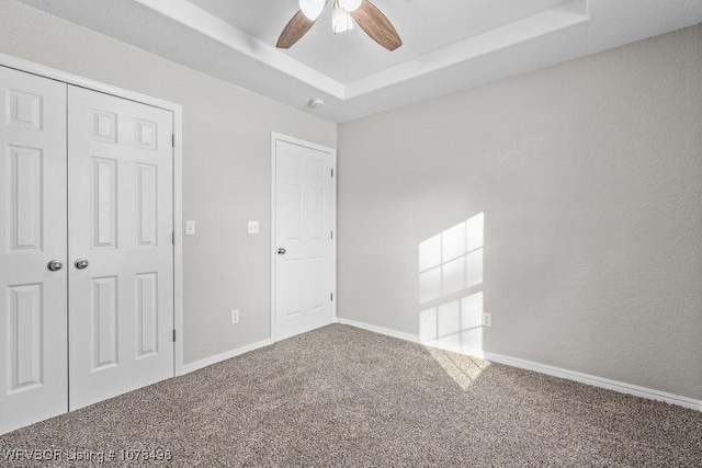 unfurnished bedroom with ceiling fan, a closet, a raised ceiling, and carpet flooring