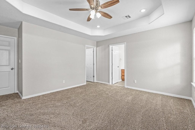 unfurnished bedroom with light carpet, ceiling fan, connected bathroom, and a tray ceiling