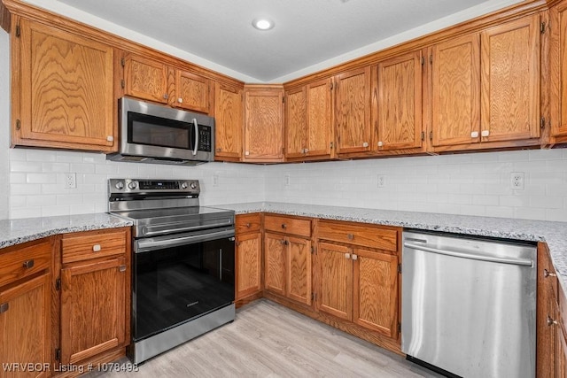 kitchen with appliances with stainless steel finishes, backsplash, light hardwood / wood-style flooring, and light stone countertops