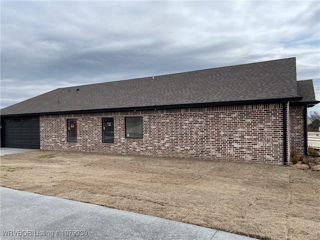 view of property exterior featuring a garage, driveway, a shingled roof, and brick siding