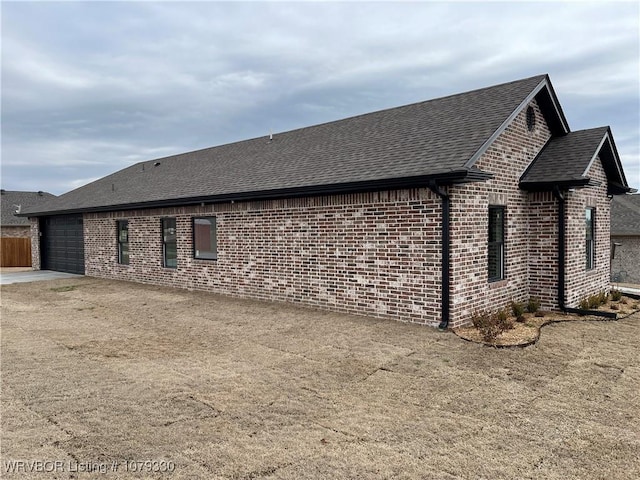 view of home's exterior featuring a garage, concrete driveway, brick siding, and roof with shingles