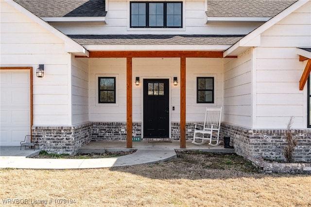 entrance to property with a shingled roof, covered porch, brick siding, and a garage