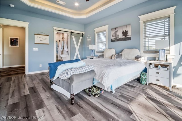 bedroom featuring dark hardwood / wood-style flooring, a barn door, and a raised ceiling