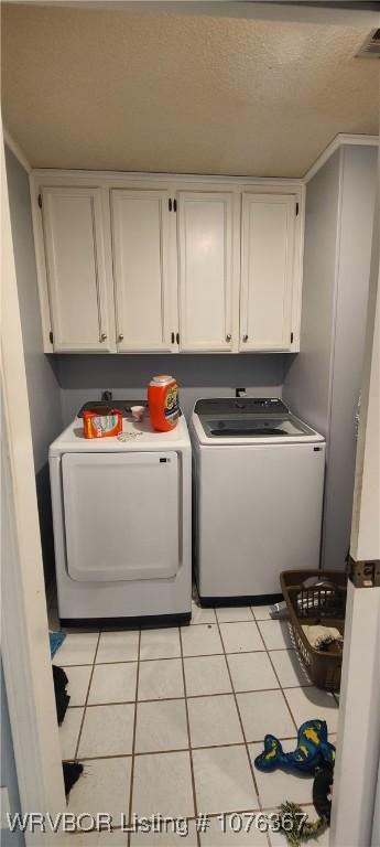 clothes washing area with washer and clothes dryer, light tile patterned floors, and cabinets