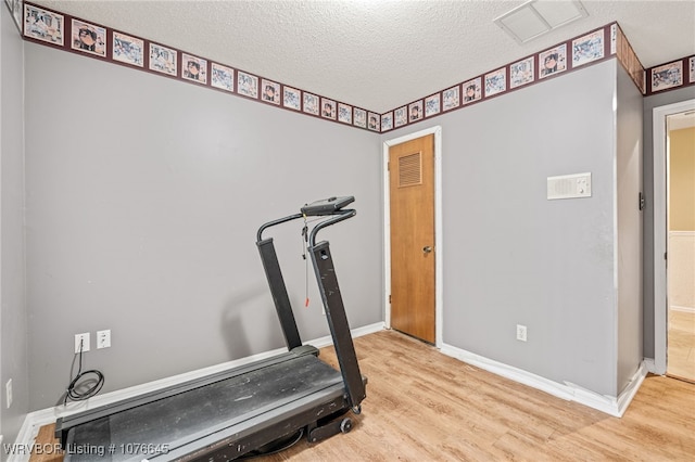 workout room featuring light wood-type flooring and a textured ceiling