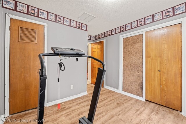 workout room with light wood-type flooring and a textured ceiling