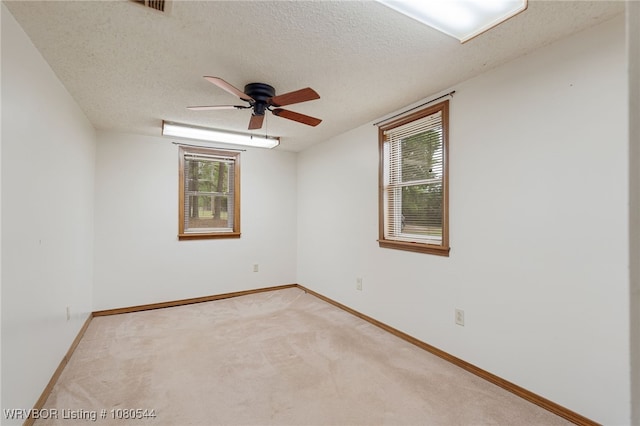 unfurnished room with a ceiling fan, visible vents, light carpet, baseboards, and a textured ceiling