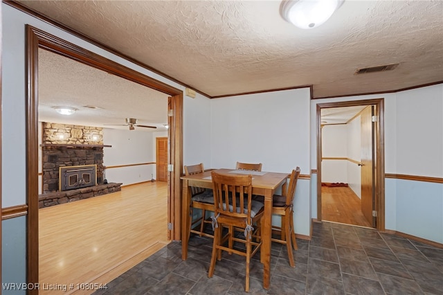 dining room featuring ceiling fan, a stone fireplace, baseboards, visible vents, and a textured ceiling