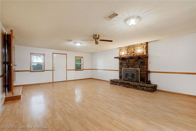 unfurnished living room with wood finished floors, a stone fireplace, baseboards, visible vents, and a ceiling fan