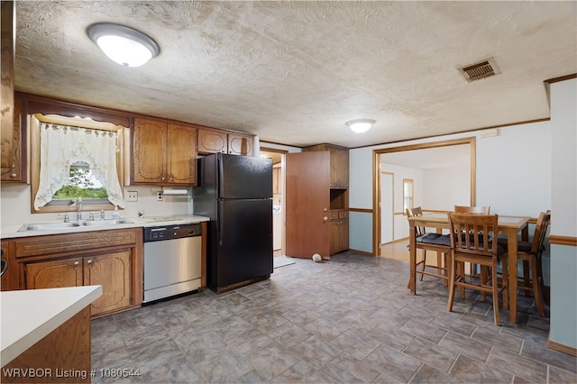 kitchen with a sink, brown cabinetry, visible vents, dishwasher, and freestanding refrigerator
