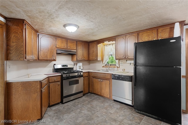 kitchen with brown cabinetry, under cabinet range hood, appliances with stainless steel finishes, light countertops, and a sink