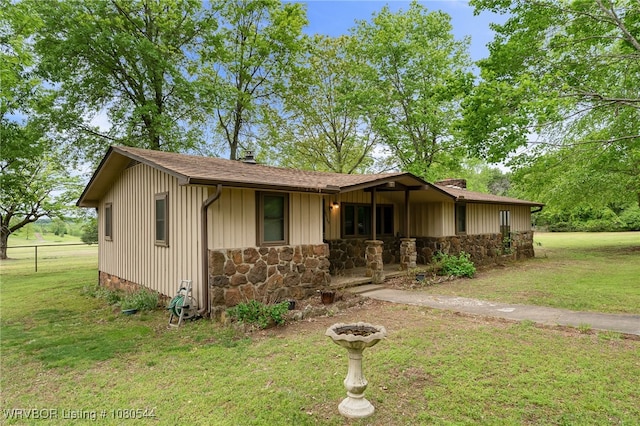 view of front of property featuring fence, roof with shingles, a front lawn, and stone siding