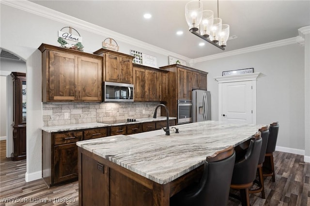 kitchen with baseboards, a sink, backsplash, a center island with sink, and appliances with stainless steel finishes