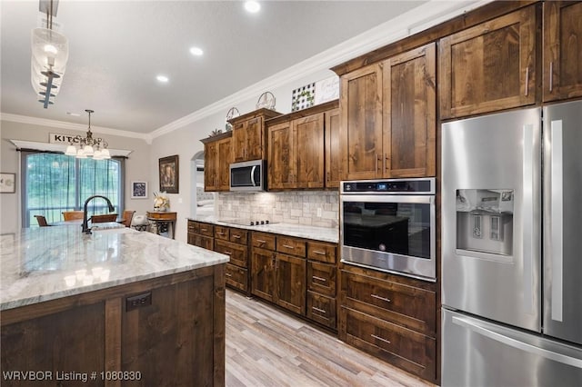 kitchen with ornamental molding, light wood finished floors, light stone counters, a sink, and stainless steel appliances