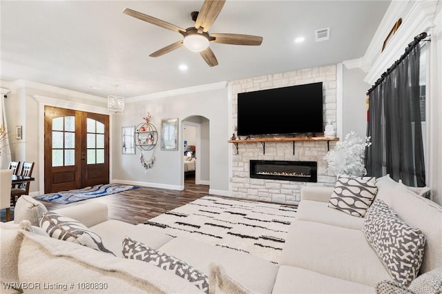 living room featuring wood finished floors, ornamental molding, visible vents, a fireplace, and ceiling fan