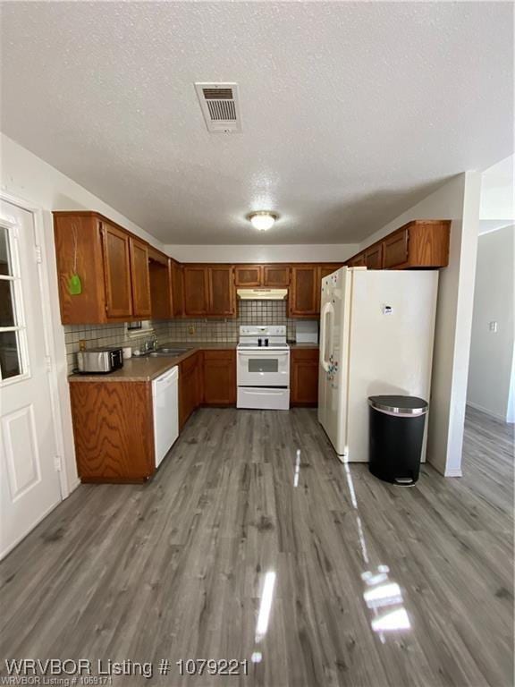 kitchen featuring under cabinet range hood, white appliances, visible vents, light wood-style floors, and brown cabinets