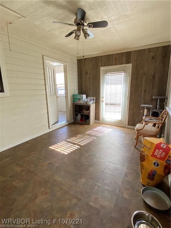 unfurnished living room featuring wood walls, a ceiling fan, and tile patterned floors