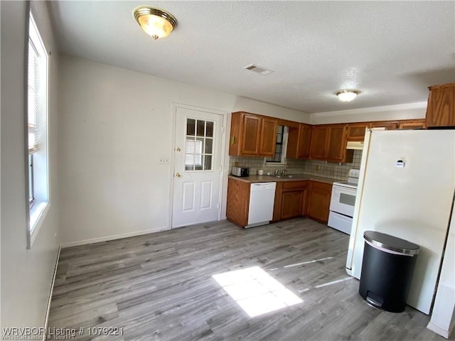 kitchen featuring tasteful backsplash, light wood-type flooring, white appliances, and visible vents