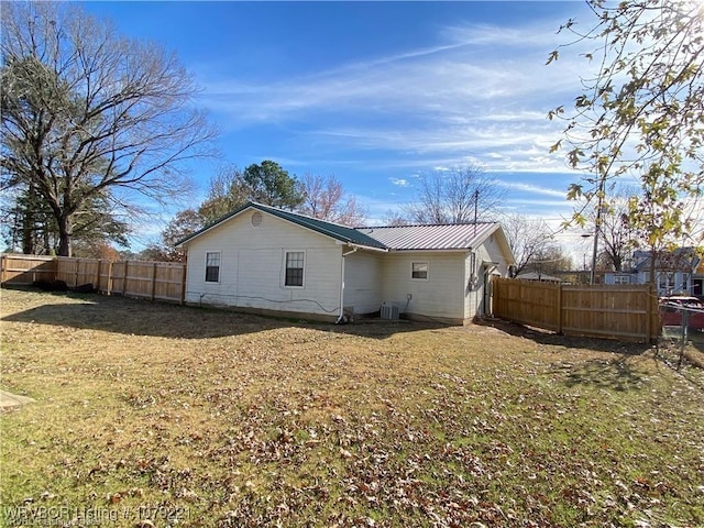 rear view of property featuring a yard, metal roof, central AC unit, and fence