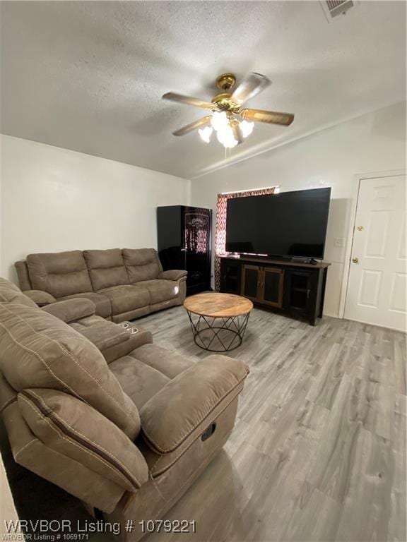 living area with lofted ceiling, light wood finished floors, ceiling fan, and a textured ceiling