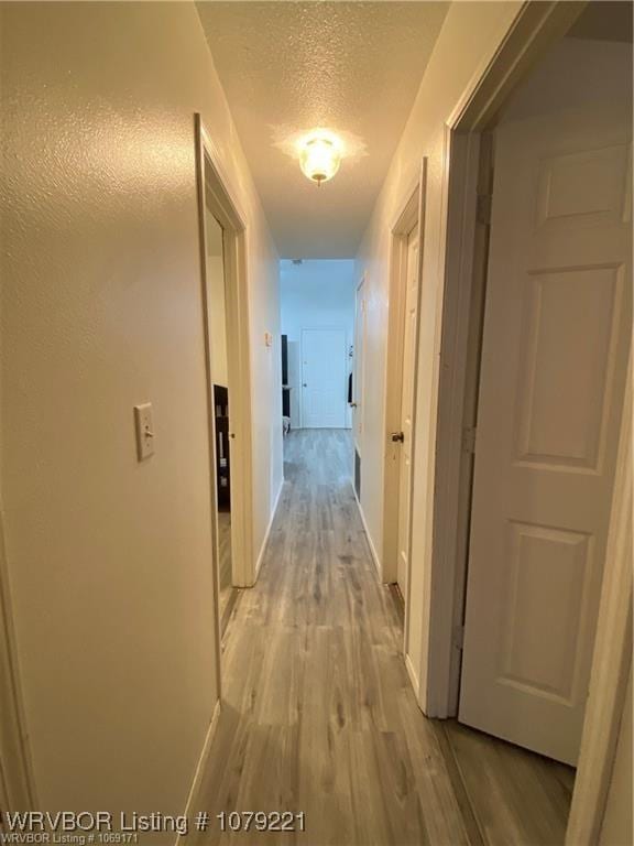 corridor with light wood-type flooring, baseboards, and a textured ceiling