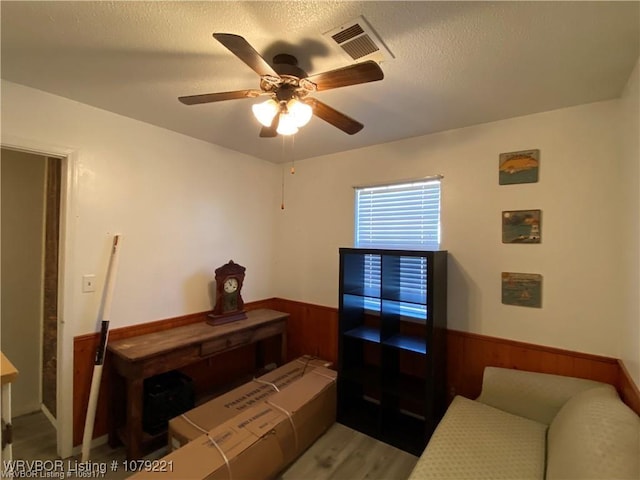 bedroom featuring a textured ceiling, wainscoting, visible vents, and wooden walls