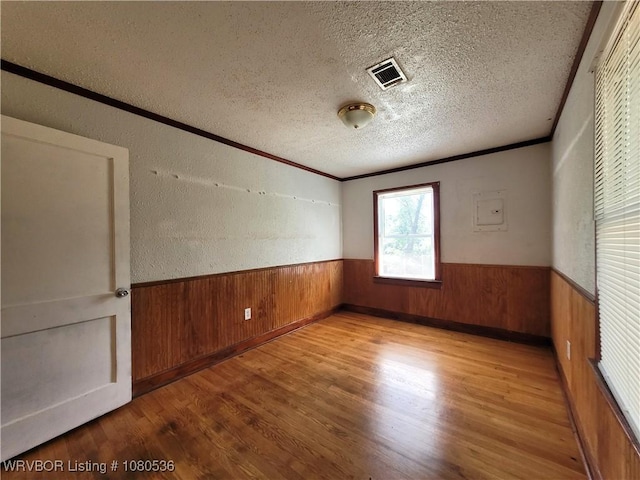unfurnished room with a wainscoted wall, a textured ceiling, visible vents, wood finished floors, and wooden walls