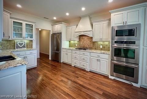 kitchen with light stone counters, tasteful backsplash, appliances with stainless steel finishes, ornamental molding, and custom exhaust hood