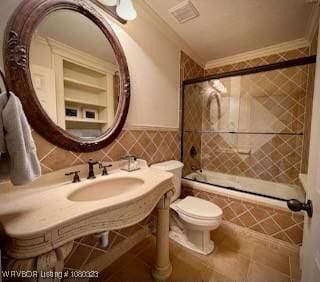bathroom featuring crown molding, a sink, tiled shower / bath, toilet, and tile walls