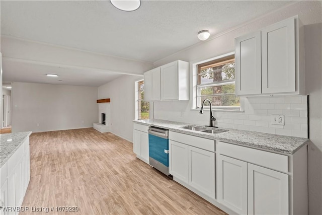 kitchen with light stone counters, a sink, white cabinetry, a brick fireplace, and dishwasher