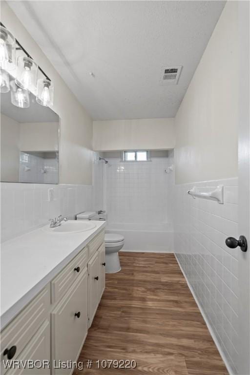 bathroom with toilet, wood finished floors, visible vents, vanity, and tile walls