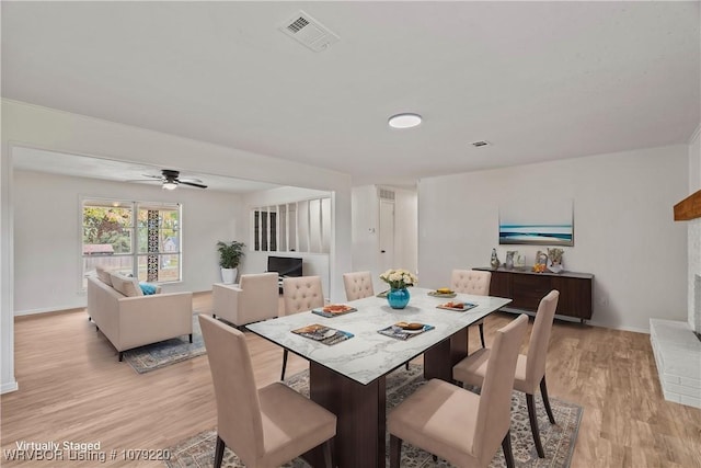 dining space with light wood-style flooring, a brick fireplace, visible vents, and baseboards