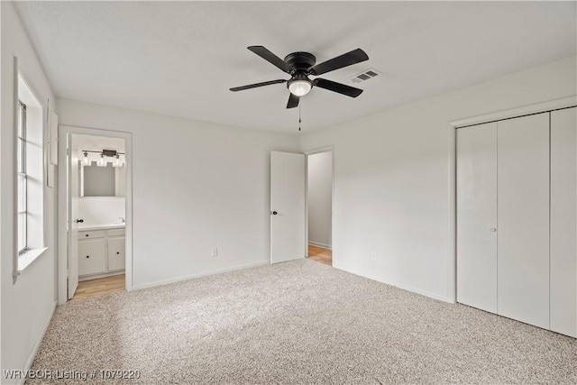 unfurnished bedroom featuring light carpet, visible vents, multiple windows, a closet, and ensuite bath