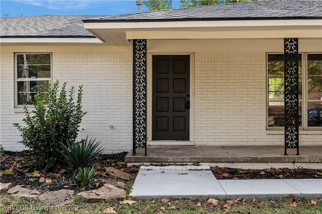 doorway to property with brick siding and roof with shingles