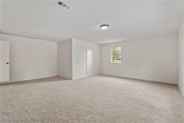 empty room featuring visible vents, a textured ceiling, attic access, and light colored carpet