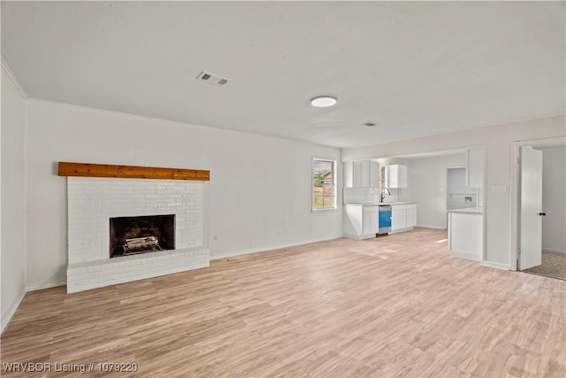 unfurnished living room featuring a sink, visible vents, baseboards, light wood-type flooring, and a brick fireplace