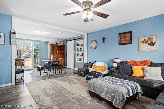 living room with ceiling fan, wood-type flooring, and a barn door