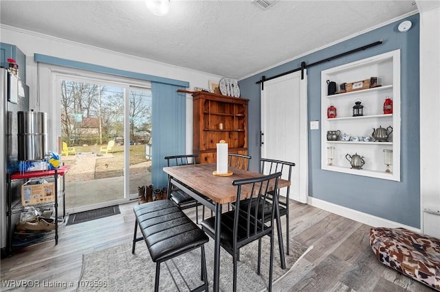 dining area featuring crown molding, wood-type flooring, a barn door, and a textured ceiling