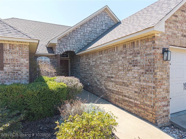 view of property exterior with brick siding, an attached garage, and roof with shingles