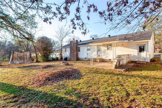 rear view of property featuring crawl space, a trampoline, a lawn, and a patio