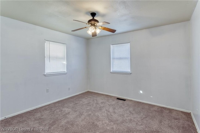 carpeted spare room featuring a ceiling fan, visible vents, and baseboards